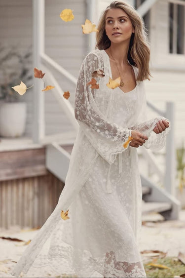 Woman in a white lace dress standing outdoors with autumn leaves falling